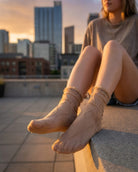 Bundled Packs Rosalie Lace Sheer Socks featuring nude sheer ankle socks with raised wavy lace texture and ruffled cuff trim, worn while seated on a rooftop ledge in warm sunset lighting, highlighting the lightweight translucent finish and delicate textured pattern.