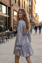 Evelina Dress sequin mini dress featuring long sleeves and open back detail, styled on a city street setting, highlighting the flowy silhouette and flattering back view.