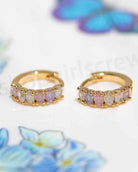 Dreaming About You Hoops featuring small gold tone hoop earrings with pastel oval stone accents and rounded prong detailing, displayed in a close up product shot over a soft floral backdrop, highlighting delicate sparkle and colorful jewelry styling.