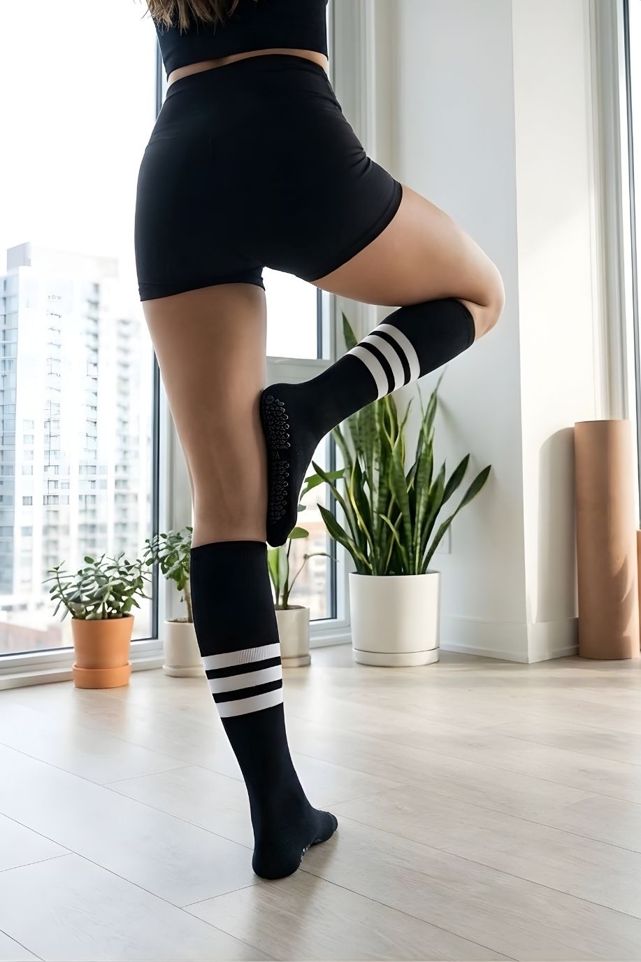 Knee High Yoga Socks featuring a stretchy, knee-high silhouette with anti-slip sole grips and contrast stripe design, shown in a close-up balance pose near large windows, highlighting traction and performance during workouts.