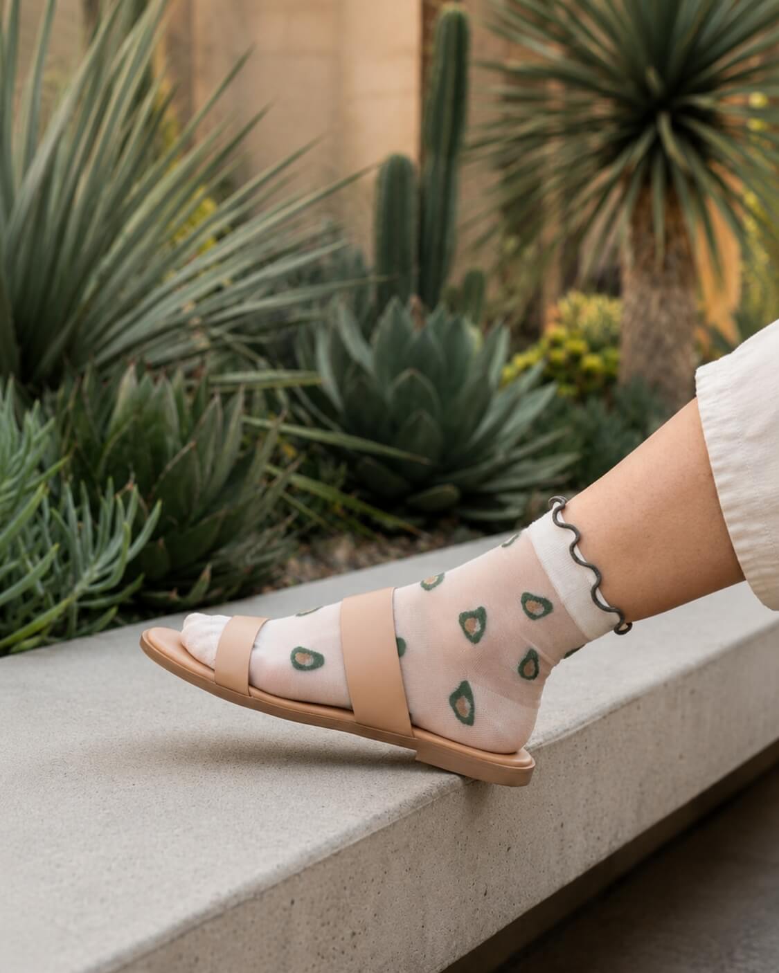 Whimsical Ruffle Edge Sheer Socks featuring a transparent ankle-length fit with avocado-inspired motifs and contrasting ruffle edging, paired with open-toe sandals in a landscaped outdoor setting, highlighting versatility and lightweight wear.