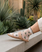 Whimsical Ruffle Edge Sheer Socks featuring a transparent ankle-length fit with avocado-inspired motifs and contrasting ruffle edging, paired with open-toe sandals in a landscaped outdoor setting, highlighting versatility and lightweight wear.