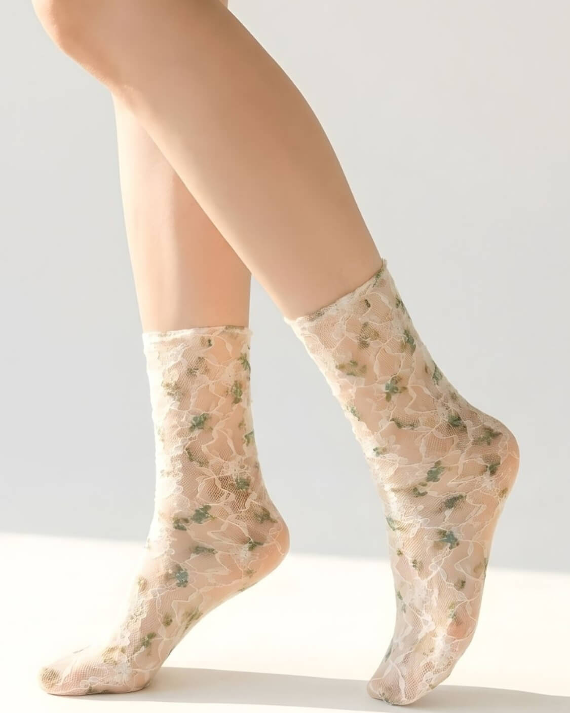 Floral mesh sheer socks in a muted green floral pattern, styled on both feet in a clean studio setting to highlight the soft mesh fabric and delicate lace details.