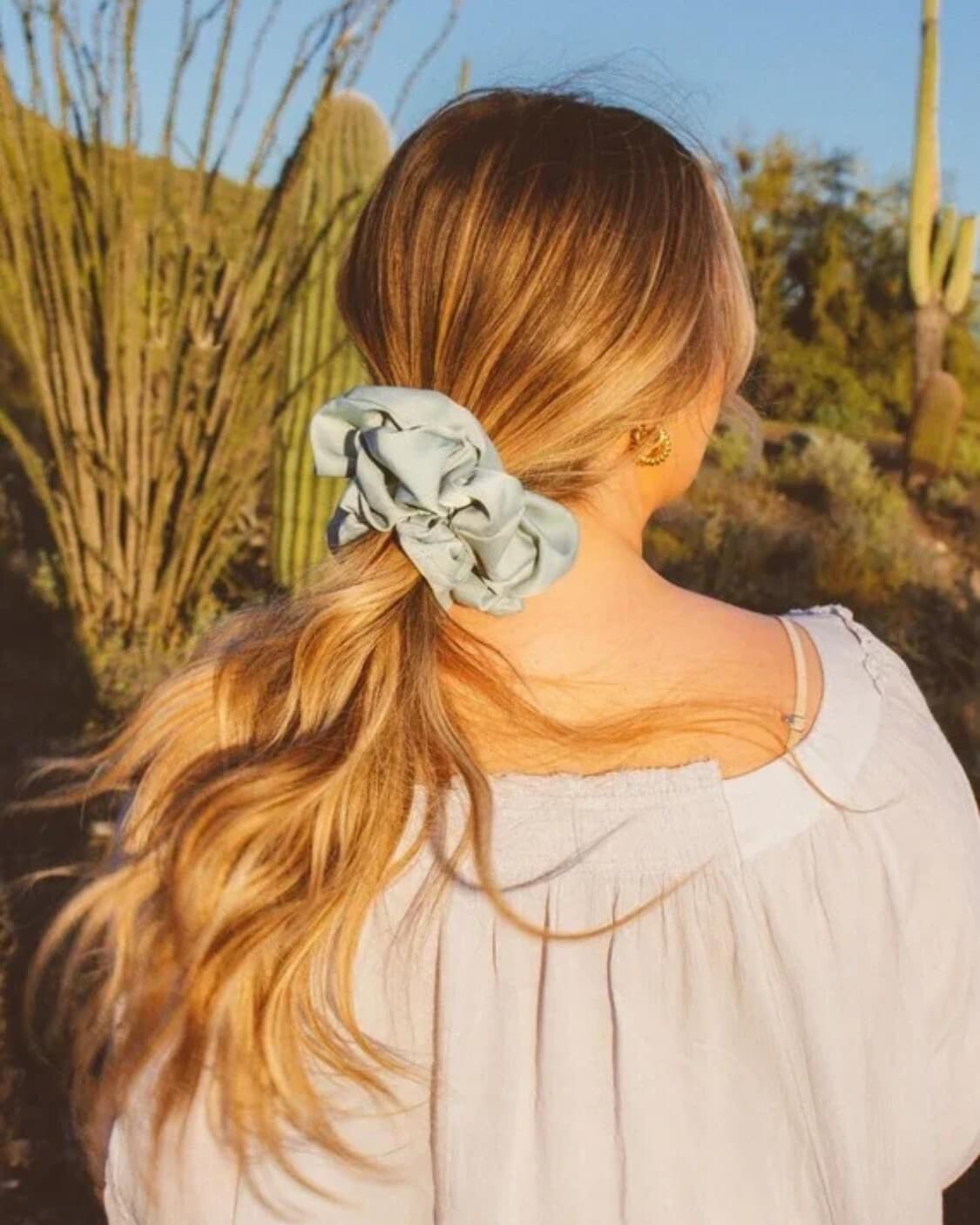 Rear view of model styling the Eucalyptus Jumbo Scrunchie highlighting the soft sateen material and eucalyptus blue green tone in a voluminous hairstyle.