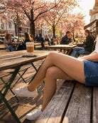 Lightweight Semi Opaque Tights in nude, featuring a smooth semi-opaque texture and even tone coverage, styled with casual sneakers and a denim skirt, shown on a model seated at an outdoor café table.