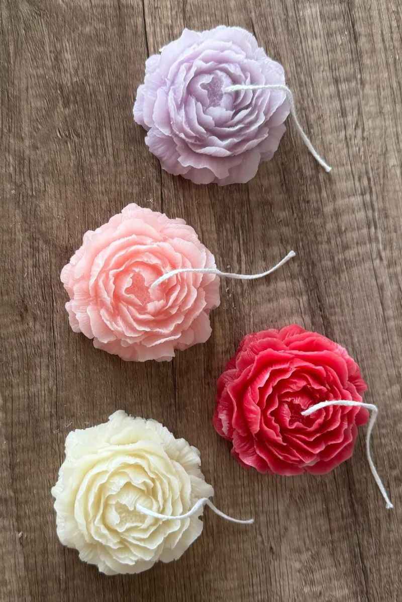 Four flower-shaped decorative candles in pastel pink, purple, cream, and red on wood surface