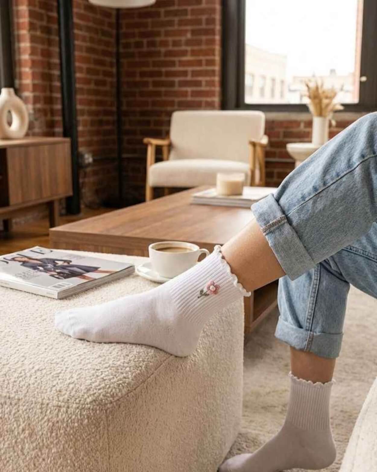 3-Pack Blush Pearl Rose Ruffle Crew Socks featuring a ribbed crew sock with a ruffled cuff and floral embroidery accent, worn with rolled cuff jeans while lounging in a cozy living room, highlighting relaxed comfort, subtle texture, and casual everyday wear.