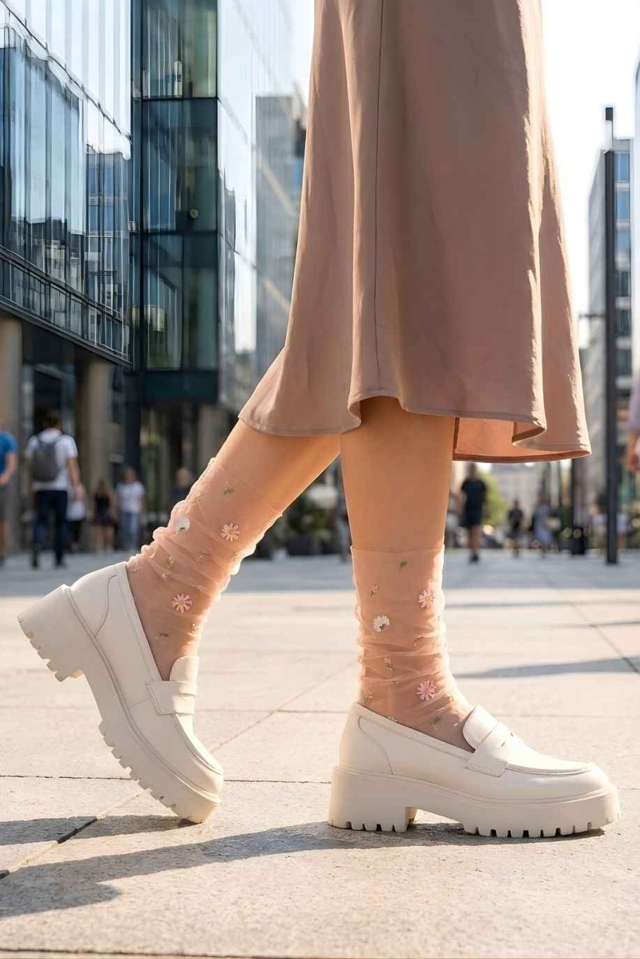 Sheer Garden Daisy Crew Socks in nude with daisy embroidery, styled with white platform loafers in an outdoor city setting for a casual look.