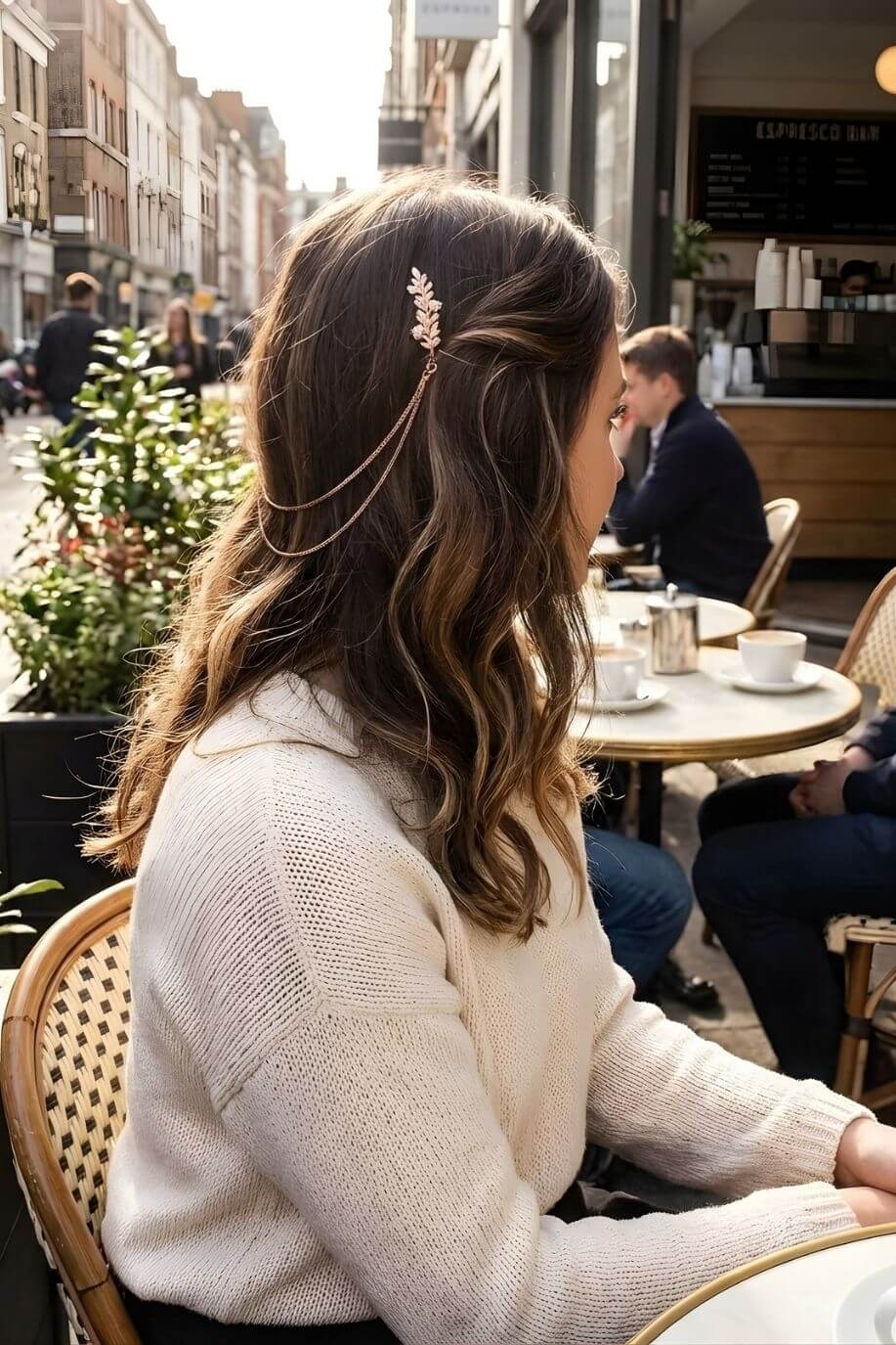 Bloom Bouquets Hair Chain featuring a gold botanical hair clip with layered chain strands, worn on softly curled hair, shown in side profile at an outdoor café with warm natural lighting.