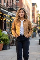 Long Sleeve Denim Jacket in tan, featuring a classic button-up front with flap chest pockets and tailored fit, paired with a white tee and dark jeans, shown on a model walking down a lively urban street with warm evening lights.