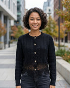 The Eloise Cardigan featuring a classic round neckline, button-front fastening, cable knit texture, and lace hem, worn outdoors on a city street, highlighting its polished finish and everyday layering style.
