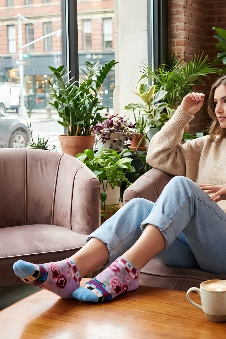 Dolce Vita Ultra-Short Sock featuring a flexible ankle length fit with bold floral artwork and geometric stripe detailing, worn during a cozy indoor lounge setting beside large windows and greenery, emphasizing softness and casual comfort.