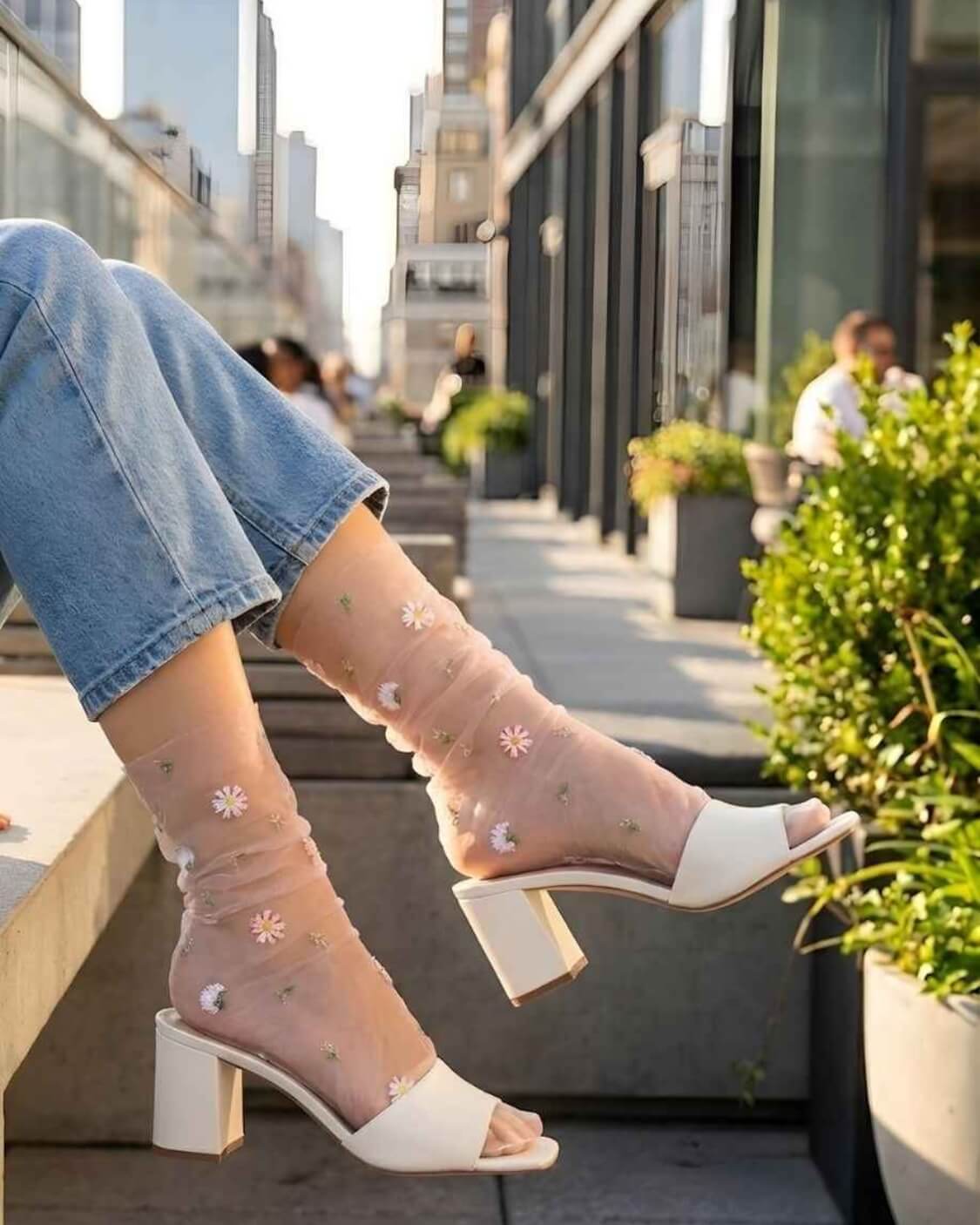 Sheer Garden Daisy Crew Socks in nude sheer fabric with embroidered daisies, styled with heeled mules and jeans in an urban setting.