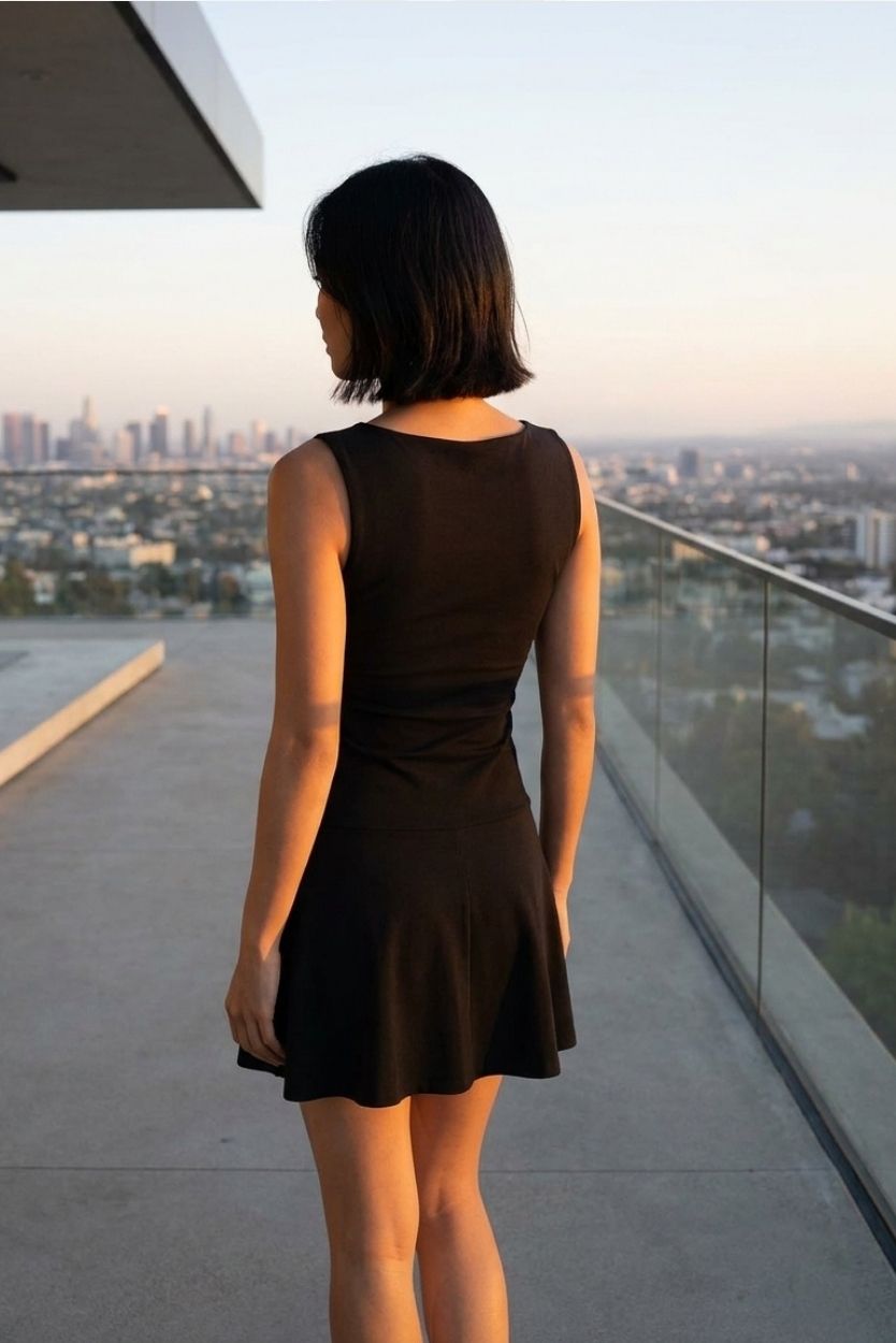 Slow Dancing Mini Dress featuring a sleeveless fitted top with flowy skirt, styled from the back on a rooftop with sunset city views, highlighting the clean back profile and graceful movement.