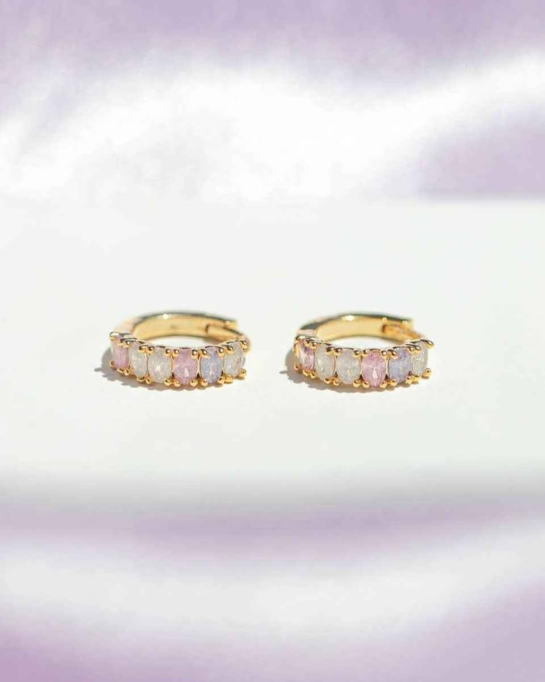 Dreaming About You Hoops featuring compact hoop earrings with pastel stone detailing and polished gold tone edges, shown on a bright reflective surface with soft purple shadows, emphasizing subtle shimmer and dainty everyday wear.