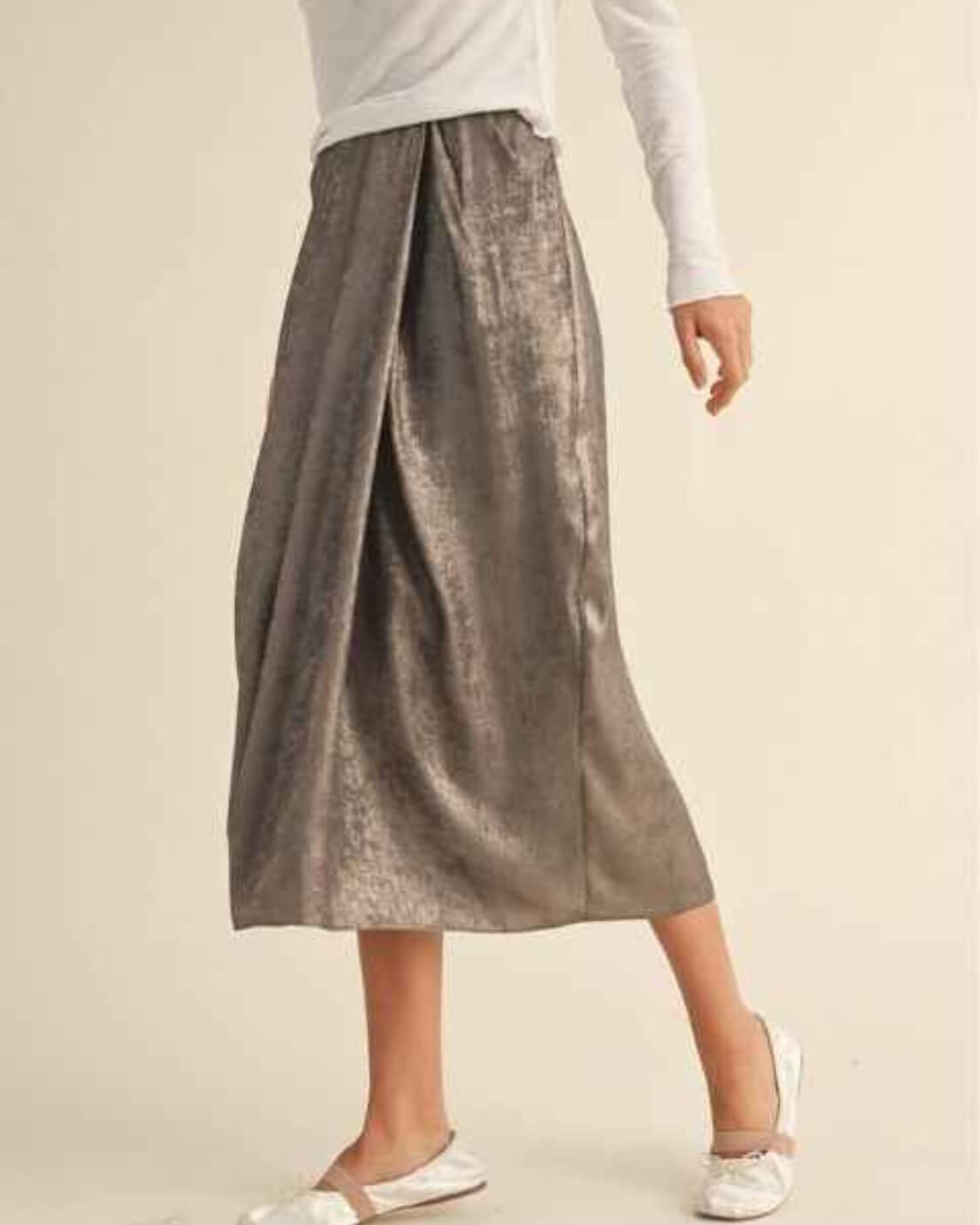 Metallic Fabric Pleat Detailed Skirt featuring a flowing midi length silhouette with soft pleated structure and subtle shimmering texture, styled with pointed bow heels in a bright minimalist interior, highlighting graceful movement and relaxed sophistication.