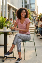 Crochet Knit Cap Sleeve Sweater Top, blush pink open-knit sweater with cap sleeves and scalloped V-neckline, styled with gray high-waisted jeans and slip-on shoes, worn by a seated model holding a coffee at a sidewalk café, showcasing the lightweight drape and casual everyday styling.