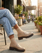 Beige sheer ribbed ankle socks with rose embroidery worn with chunky loafers and rolled jeans, styled outdoors on a city sidewalk café.