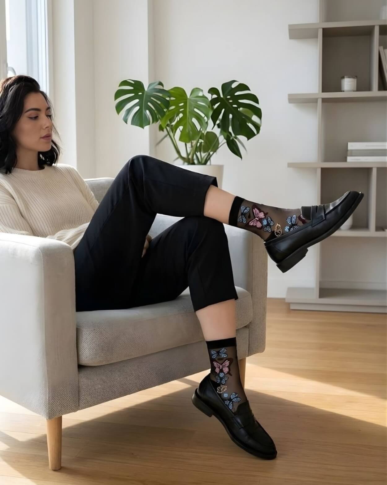 Butterfly Sheer Socks 2-Pack featuring transparent mesh fabric with intricate butterfly designs, styled in black paired with loafers while seated in a minimalist living room.