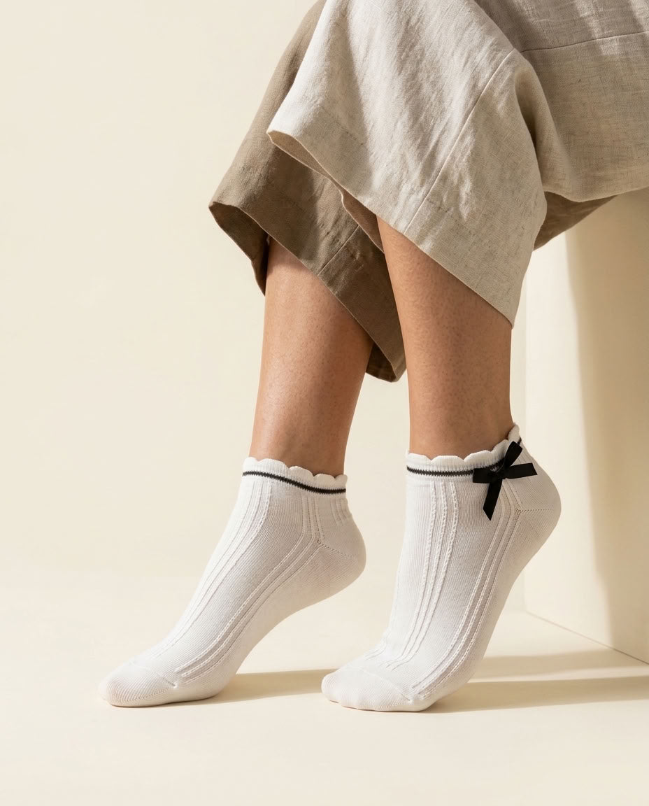 White ribbed ankle socks with scalloped cuff, black stripe and black satin bow, close-up on tiptoe