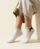 White ribbed ankle socks with scalloped cuff, black stripe and black satin bow, close-up on tiptoe
