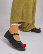 Cherry Accent Mary Jane Flats, black woven Mary Jane flats with cherry detail and buckle strap, paired with a textured olive-green dress and minimal anklet, showcasing a relaxed yet playful daytime look.
