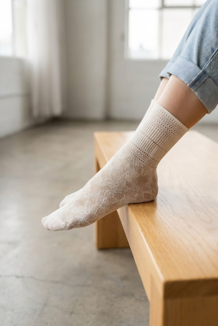 Sheer Floral Lace Crew Socks in ivory with intricate lace floral pattern, worn with rolled cuff jeans while resting on a wooden bench indoors, highlighting the delicate texture and lightweight feel.