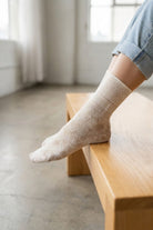 Sheer Floral Lace Crew Socks in ivory with intricate lace floral pattern, worn with rolled cuff jeans while resting on a wooden bench indoors, highlighting the delicate texture and lightweight feel.