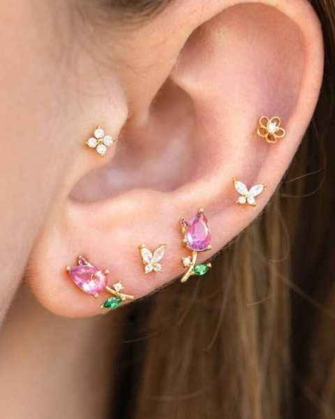 Blossoming Tulip Studs featuring floral tulip inspired crystal studs with gold tone stems and sparkling leaf accents, styled in a curated ear stack with butterfly and flower earrings, emphasizing playful botanical styling and layered jewelry detail.