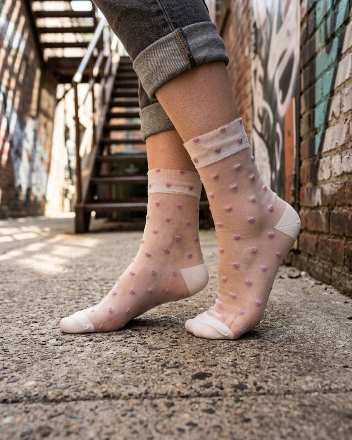 Blushing Hearts Sheer Socks featuring sheer ankle socks with raised pastel heart accents and soft toe panels, worn outdoors in an urban walkway setting, highlighting the delicate transparent texture and playful dotted heart detailing.