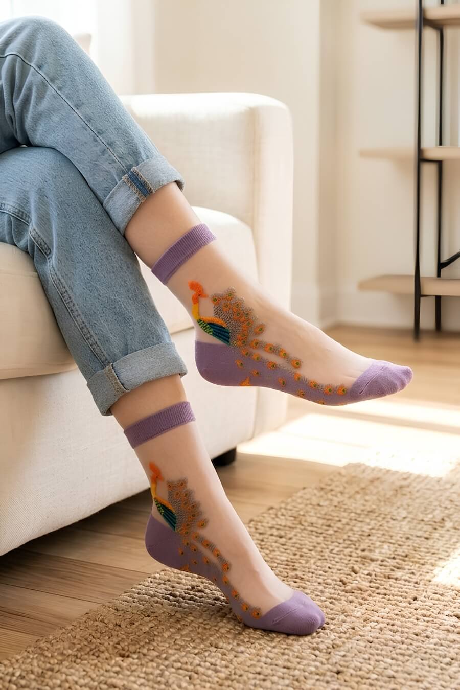 Peacock Sheer Mesh Socks featuring soft lavender accents with transparent mesh panels and ornate peacock embroidery in multicolor thread, worn indoors with rolled cuff jeans while relaxing on a sofa in a cozy sunlit living room, highlighting everyday comfort, breathable material, and playful decorative style.