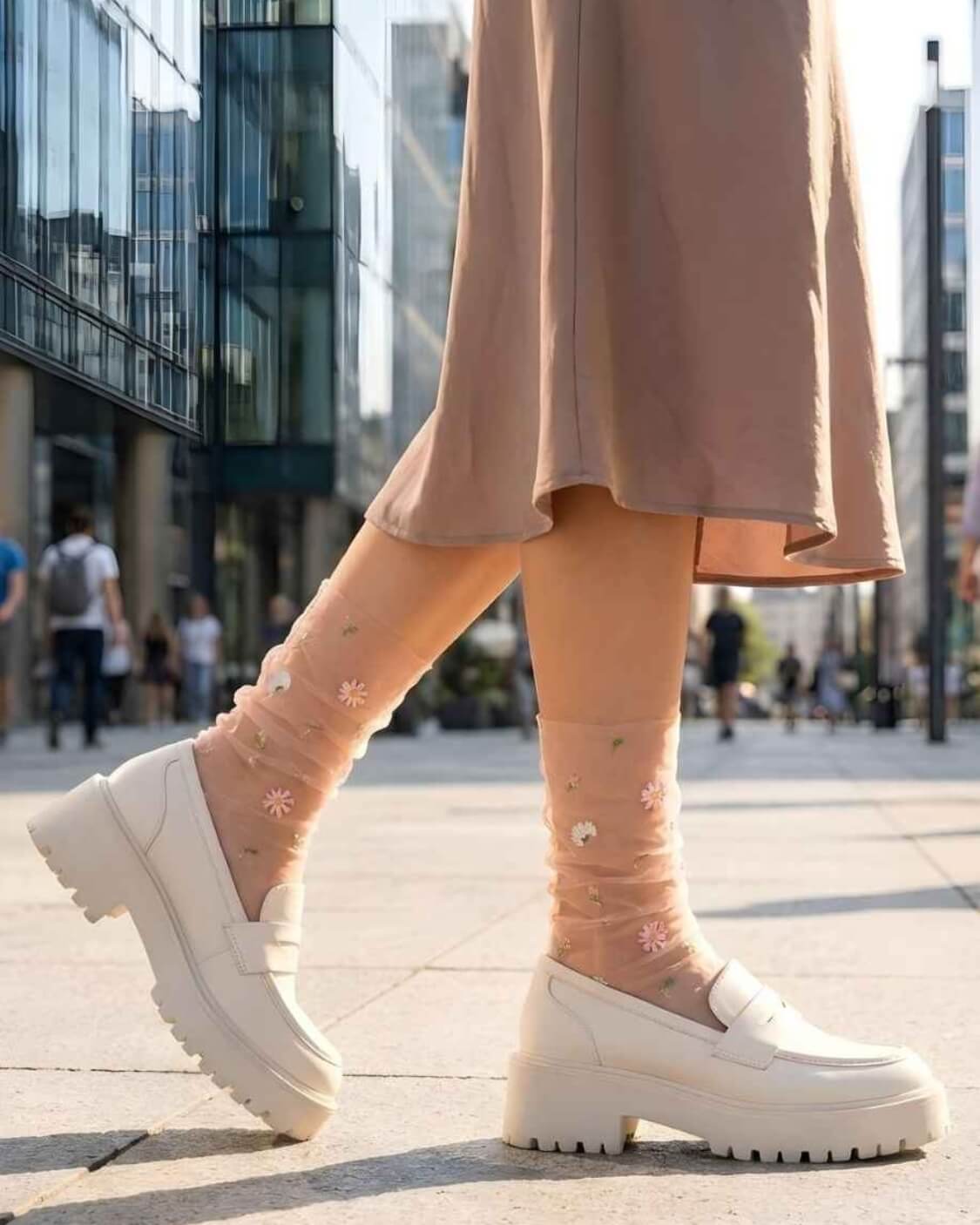 Sheer Garden Daisy Crew Socks in nude with daisy embroidery, styled with white platform loafers in an outdoor city setting for a casual look.