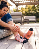 Shorty Socks, Wine Down featuring a short ankle cut, wine-themed pattern, dark toe accents, and “Down” text on the sole, worn while adjusting the cuff on a patio deck, highlighting the graphic sole and snug fit.