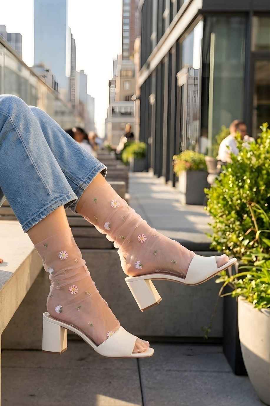 Sheer Garden Daisy Crew Socks in nude sheer fabric with embroidered daisies, styled with heeled mules and jeans in an urban setting.