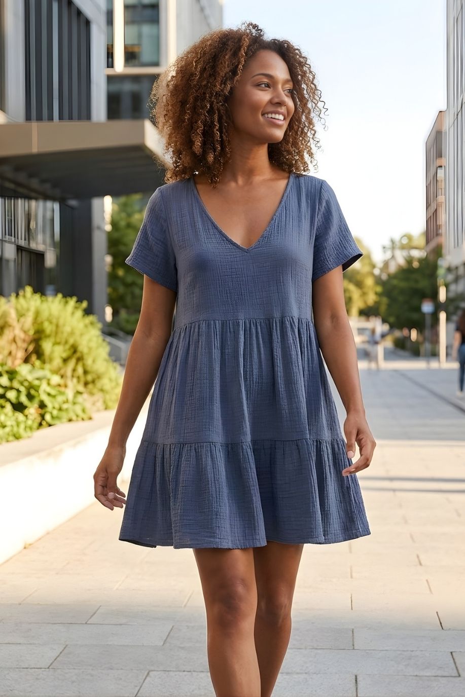 Cassady Dress featuring a breezy, relaxed fit with a V-neckline, short sleeves, and tiered hem, styled on a sunny city street with modern buildings and greenery.