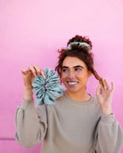 Model wearing the Eucalyptus Jumbo Scrunchie against a pink background, featuring oversized sateen fabric and soft eucalyptus green color.