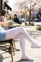 Lightweight Semi Opaque Tights in white, featuring a smooth lightweight construction and uniform coverage, styled casually with sneakers and a skirt, shown on a model seated at an outdoor café.