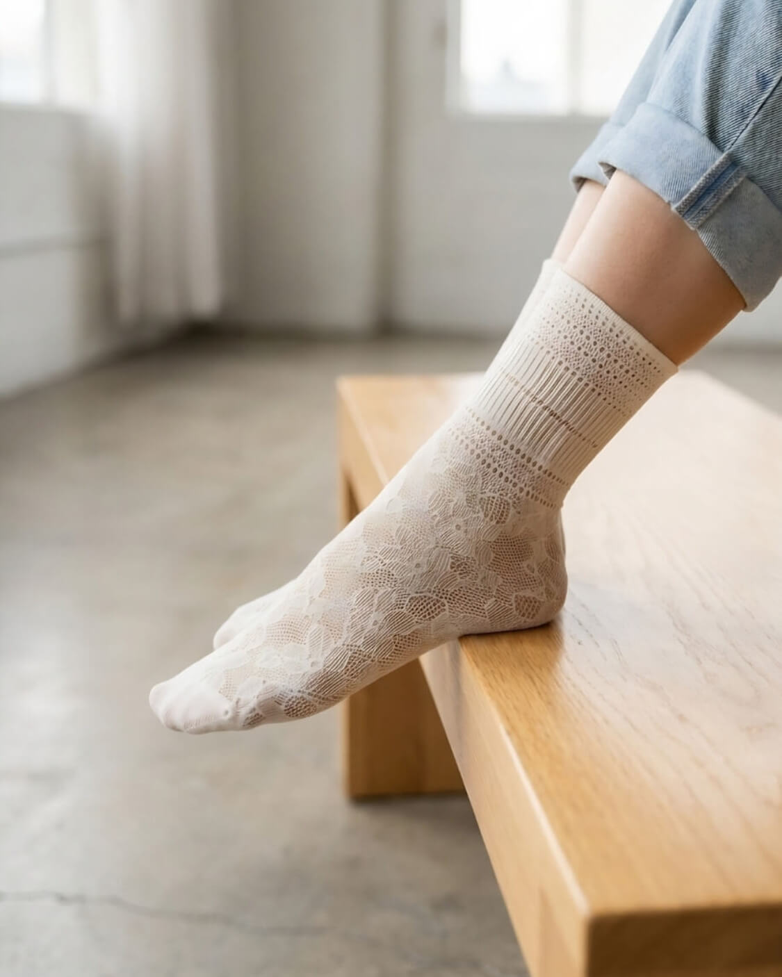 Sheer Floral Lace Crew Socks in ivory with intricate lace floral pattern, worn with rolled cuff jeans while resting on a wooden bench indoors, highlighting the delicate texture and lightweight feel.