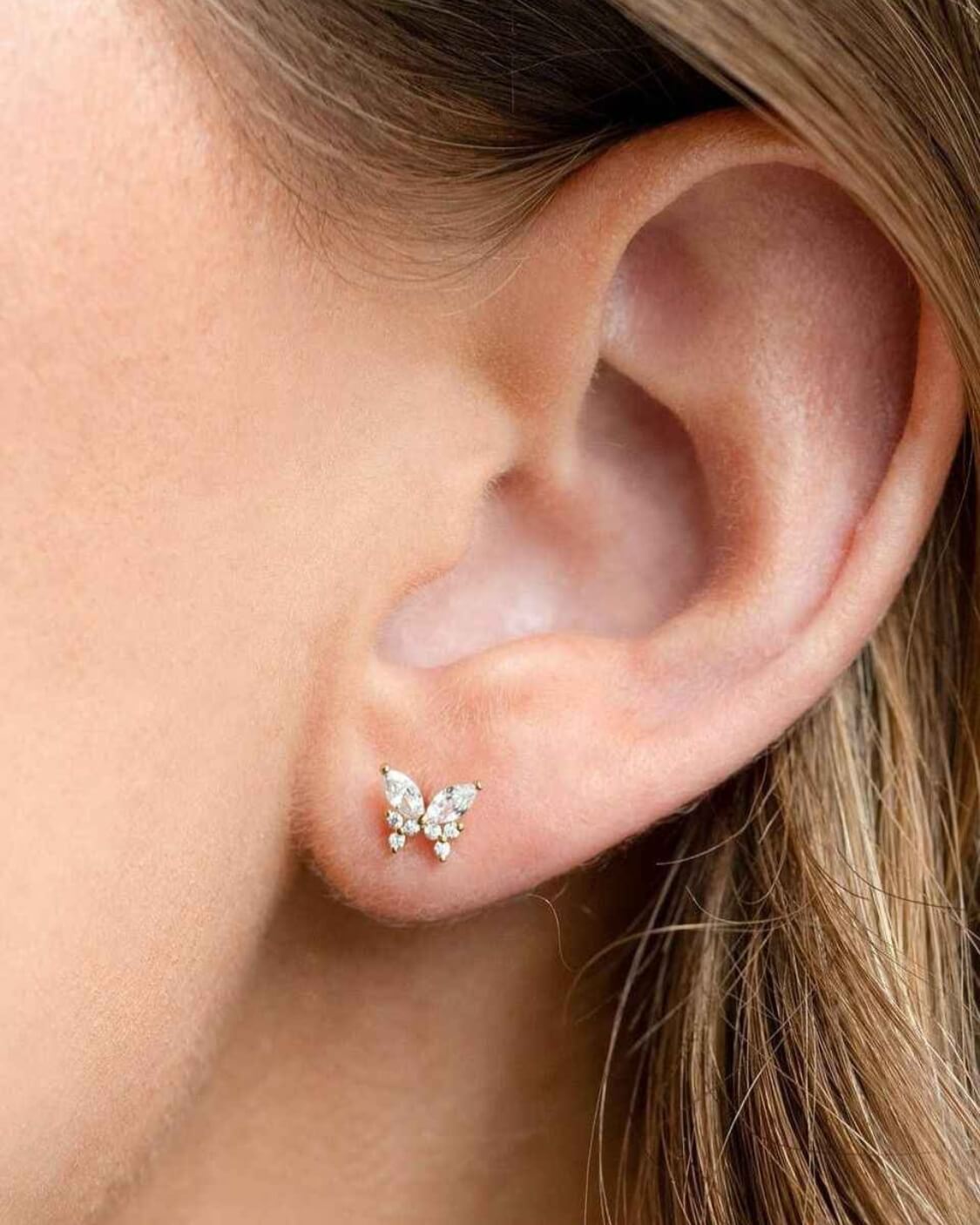 Remember Me Butterfly Studs featuring a compact butterfly silhouette with crystal embellished detailing and a polished metallic finish, shown in a close up ear styling shot against soft natural lighting, highlighting delicate sparkle and refined stud placement.