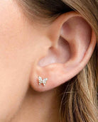 Remember Me Butterfly Studs featuring a compact butterfly silhouette with crystal embellished detailing and a polished metallic finish, shown in a close up ear styling shot against soft natural lighting, highlighting delicate sparkle and refined stud placement.