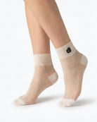 Close-up of cream sheer ribbed ankle socks with contrasting rose embroidery, shown on crossed feet against a plain white background to emphasize texture and transparency.
