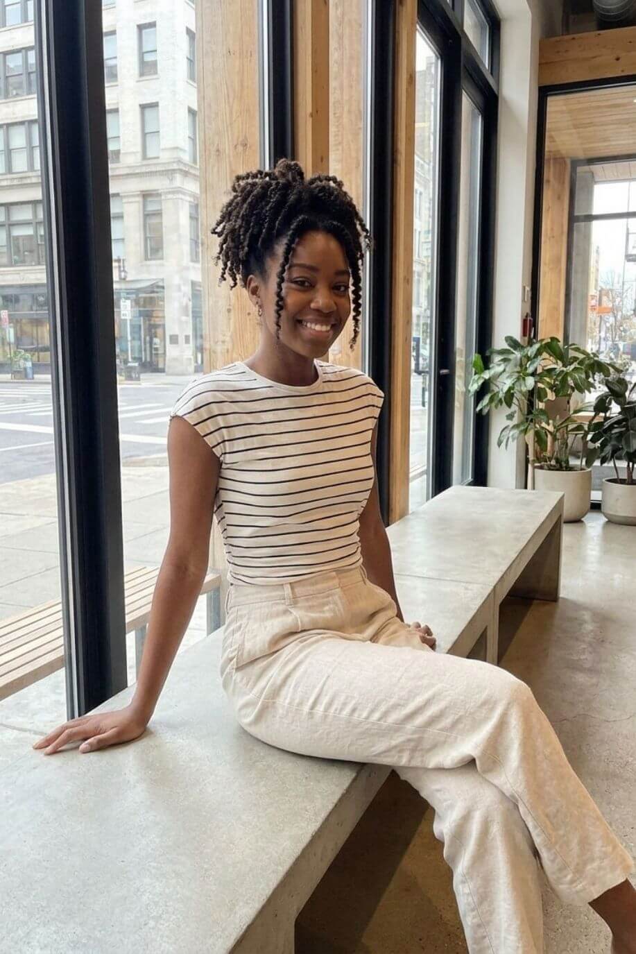 Striped Sleeveless Open Back Tank, cream and black striped sleeveless top with a crew neckline and open back detail, styled with high-waisted light trousers, worn by a seated model indoors, highlighting the casual versatility and comfortable fit.