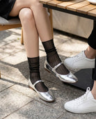 Sparkle Pinstripe Sheer Socks featuring a breathable sheer knit texture with shimmering vertical pinstripe accents and delicate stretch support, paired with silver flats in an outdoor café setting, highlighting refined comfort and chic everyday wear.