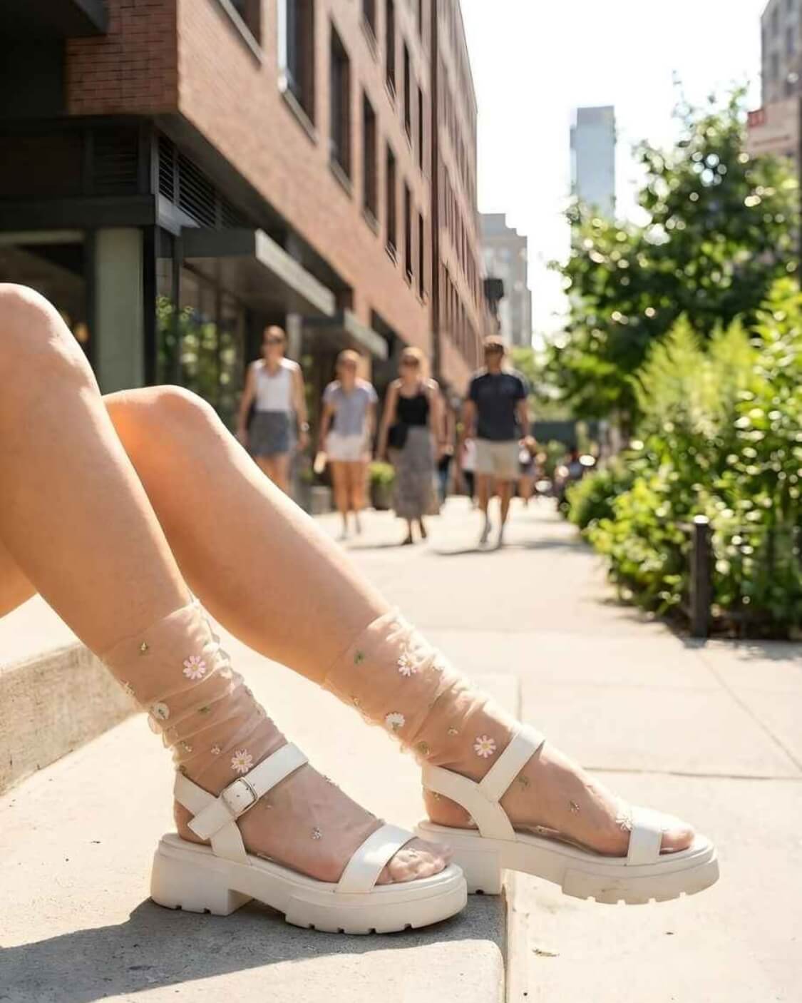 Sheer Garden Daisy Crew Socks in nude mesh with daisy details, worn with chunky white sandals while seated outdoors for a relaxed summer style.