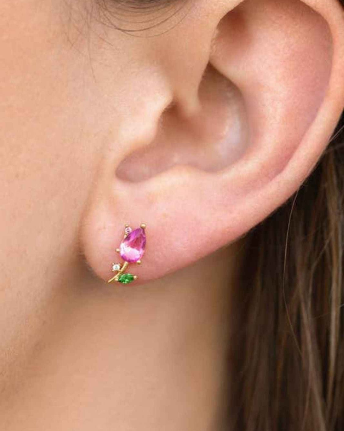 Blossoming Tulip Studs featuring a pink tulip inspired crystal shape with green leaf accents and polished gold tone detailing, worn in a close up ear styling shot against soft natural lighting, highlighting delicate floral charm and elegant everyday wear.