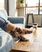 Butterfly Sheer Socks 2-Pack featuring lightweight sheer material with colorful butterfly embroidery, styled in a cream tone while lounging on a sofa with a coffee table and window-lit background.