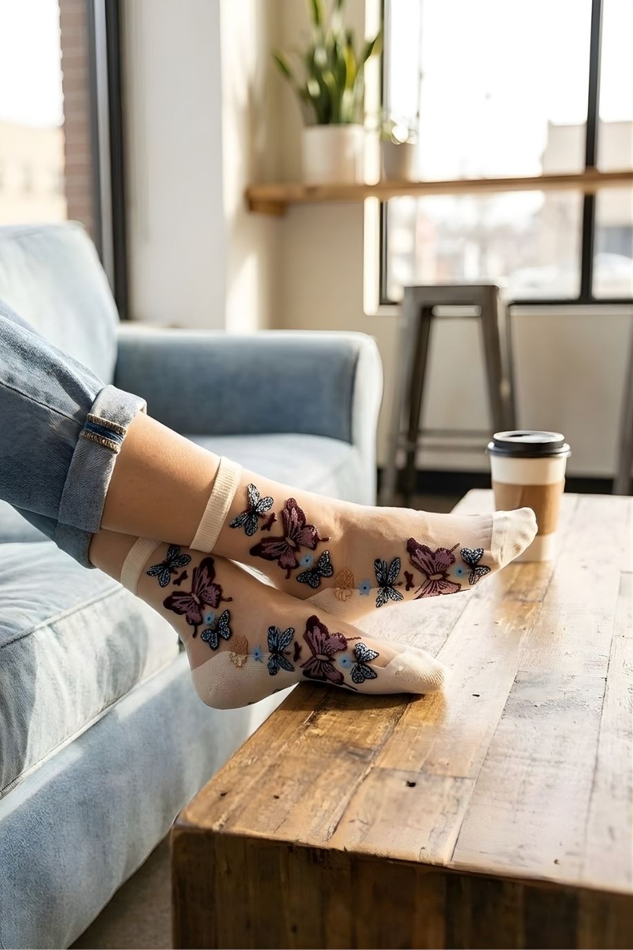 Butterfly Sheer Socks 2-Pack featuring lightweight sheer material with colorful butterfly embroidery, styled in a cream tone while lounging on a sofa with a coffee table and window-lit background.