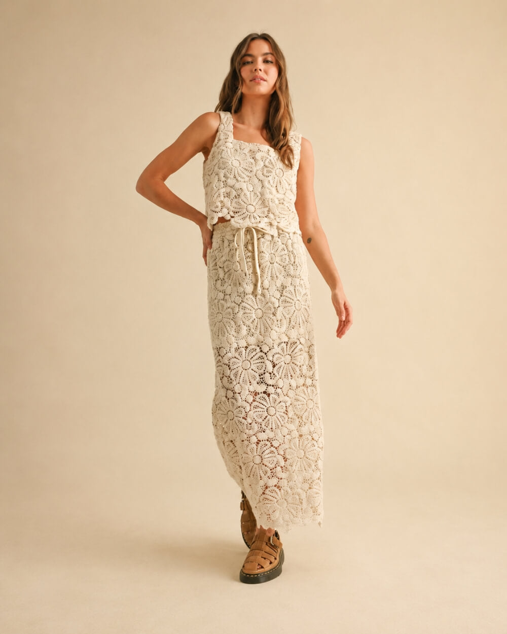 Crochet Knitted Skirt featuring oversized floral crochet detailing with a relaxed sleeveless top and adjustable drawstring waist, worn in a walking pose with woven buckle sandals in a clean studio environment, emphasizing movement comfort and intricate pattern styling.