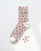 Blushing Hearts Sheer Socks featuring a sheer ankle sock with raised red heart accents, soft cuff, toe and heel panels, displayed flat on a clean studio background with small heart props, highlighting the playful heart texture and lightweight finish.