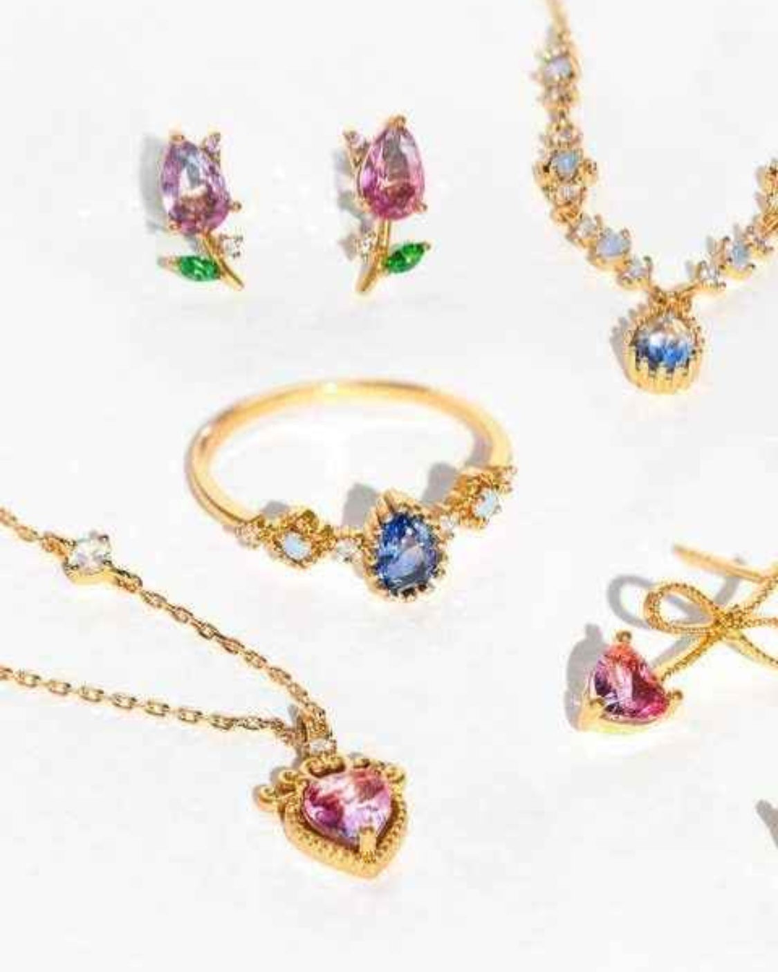 Blossoming Tulip Studs featuring pink crystal tulip earrings displayed alongside coordinating gemstone rings and necklaces on a bright reflective surface, highlighting delicate sparkle and romantic floral jewelry styling.